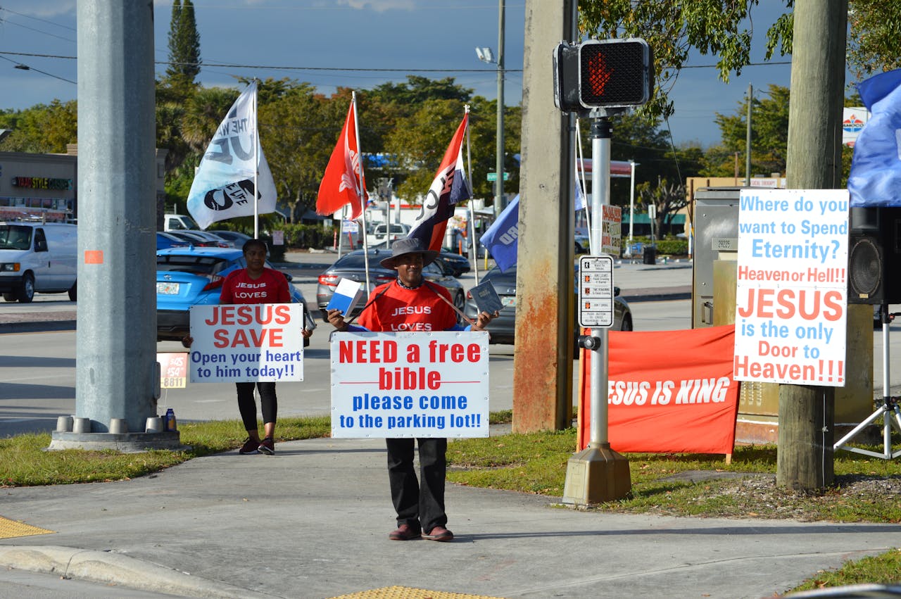 People handing out free Bibles with religious signs and flags on a city street.